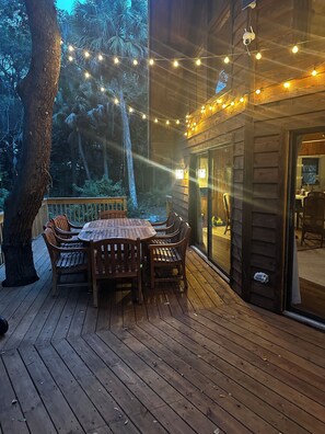 Eine Holzterrasse mit Tisch und Stühlen, umgeben von Bäumen und Lichterketten.