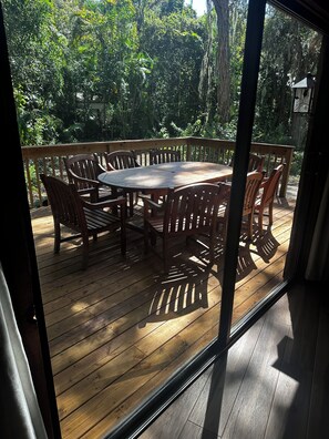 A wooden deck with a round table and chairs, surrounded by lush greenery.