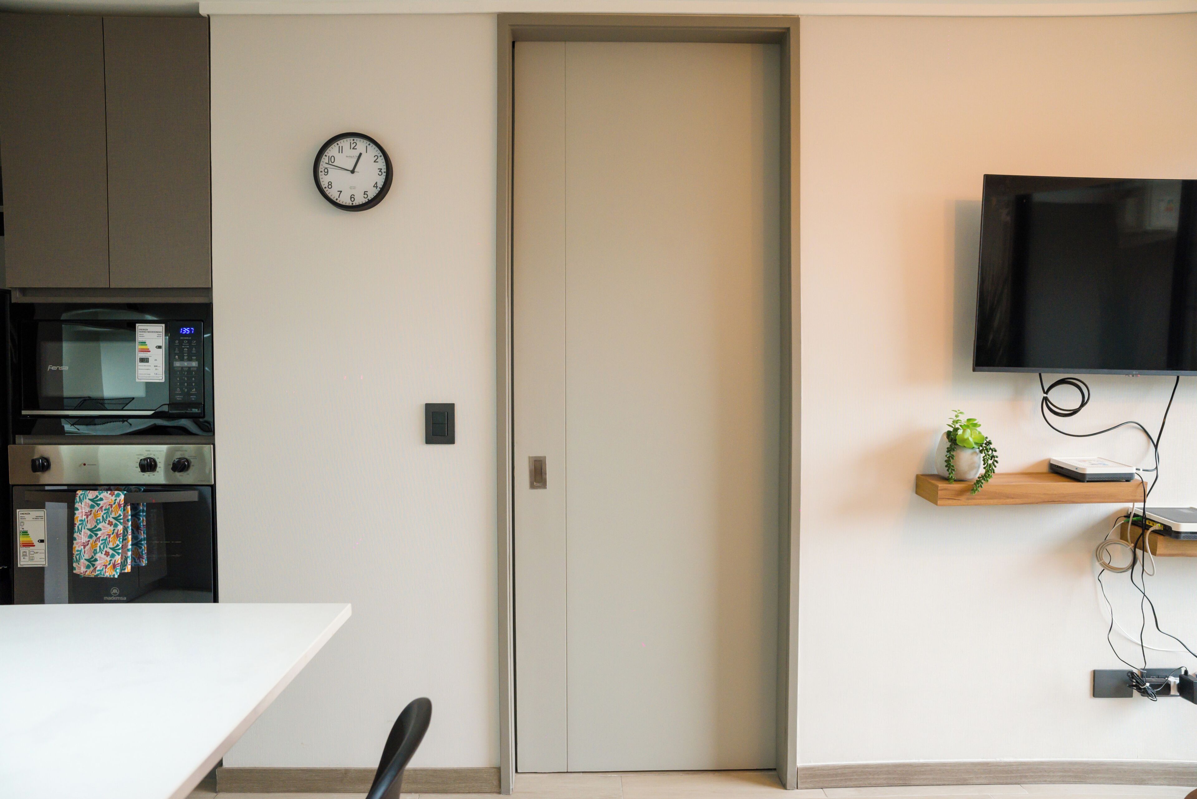 A modern kitchen with a microwave, oven, and a clock on the wall.