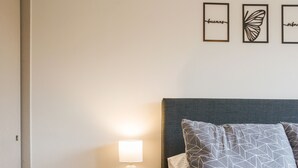 Ein Schlafzimmer mit einem Bett, einem Nachttisch, einer Lampe, Wandkunst und einem gemusterten Teppich.
