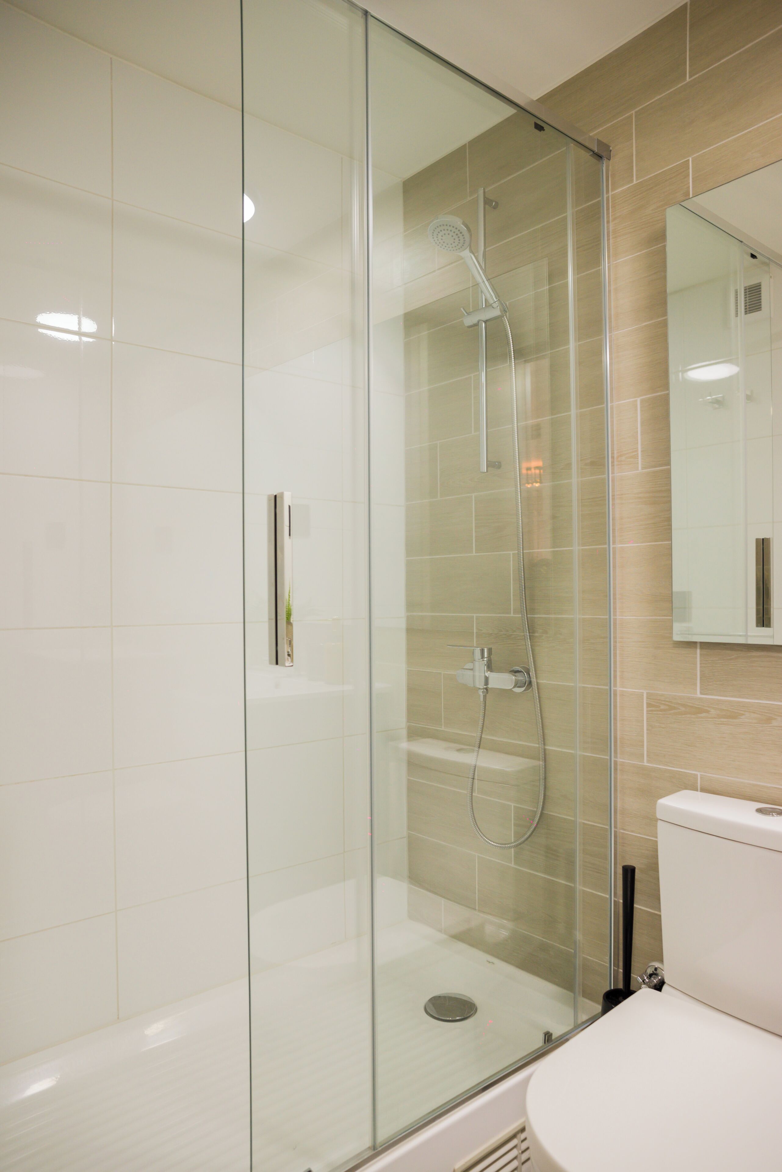 A modern bathroom with a glass-enclosed shower, a toilet, and a mirror on the wall.