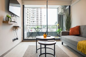 A modern living room with a grey sofa, a round table, and a balcony with a view of a high-rise building. - Brown Sur Apartments by Andes STR (Ñuñoa)