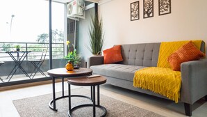 Ein modernes Wohnzimmer mit einem grauen Sofa, einem gelben Wurfdecken und einem kleinen runden Tisch mit einer Pflanze.
