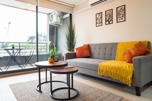 Ein modernes Wohnzimmer mit einem grauen Sofa, einem gelben Wurfdecken und einem kleinen runden Tisch mit einer Pflanze.