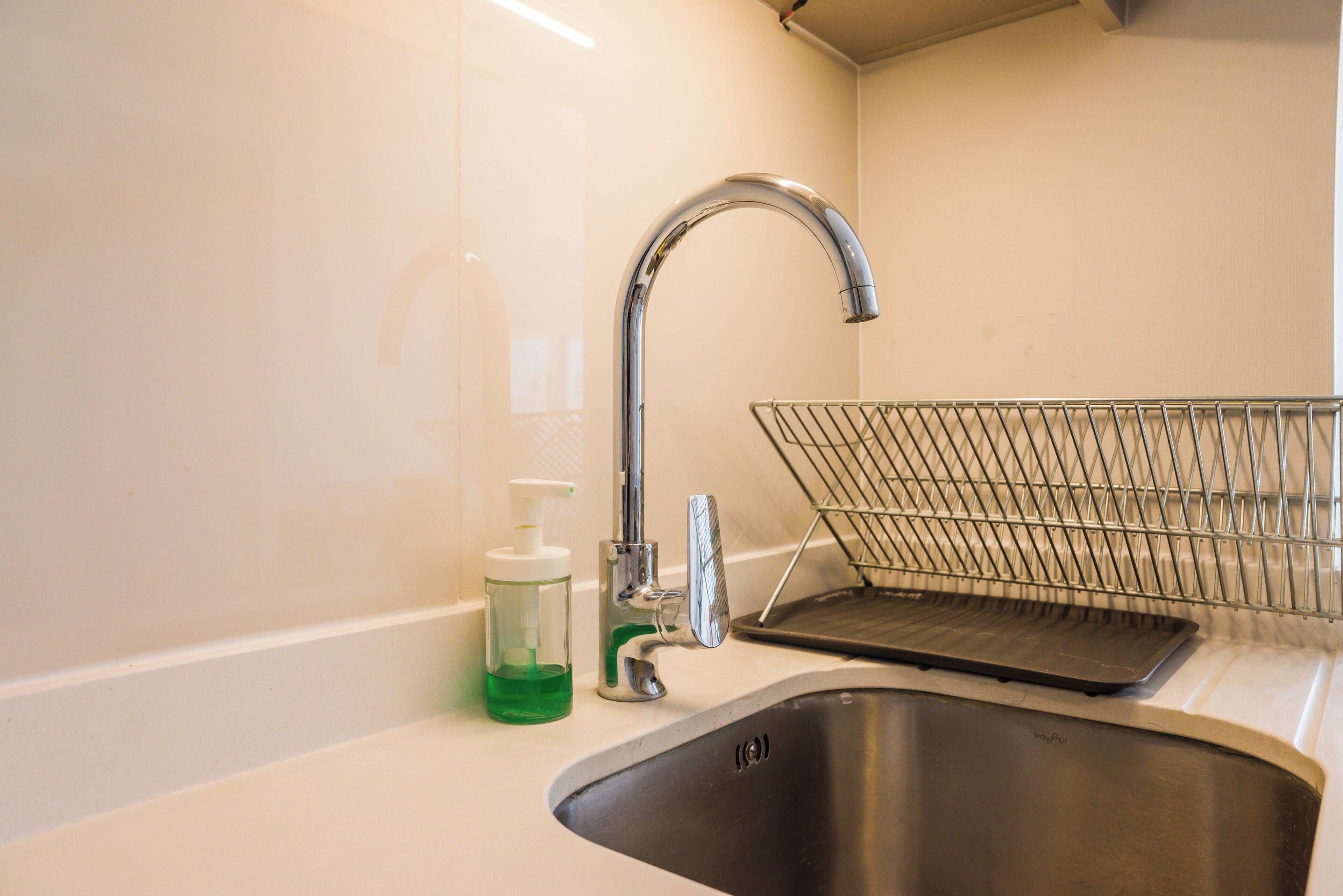 A stainless steel sink with a modern faucet, a soap dispenser, and a metal drying rack.