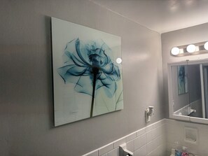Ein Badezimmer mit einem wandmontierten Spiegel, einem Waschbecken und einem blauen abstrakten Gemälde.