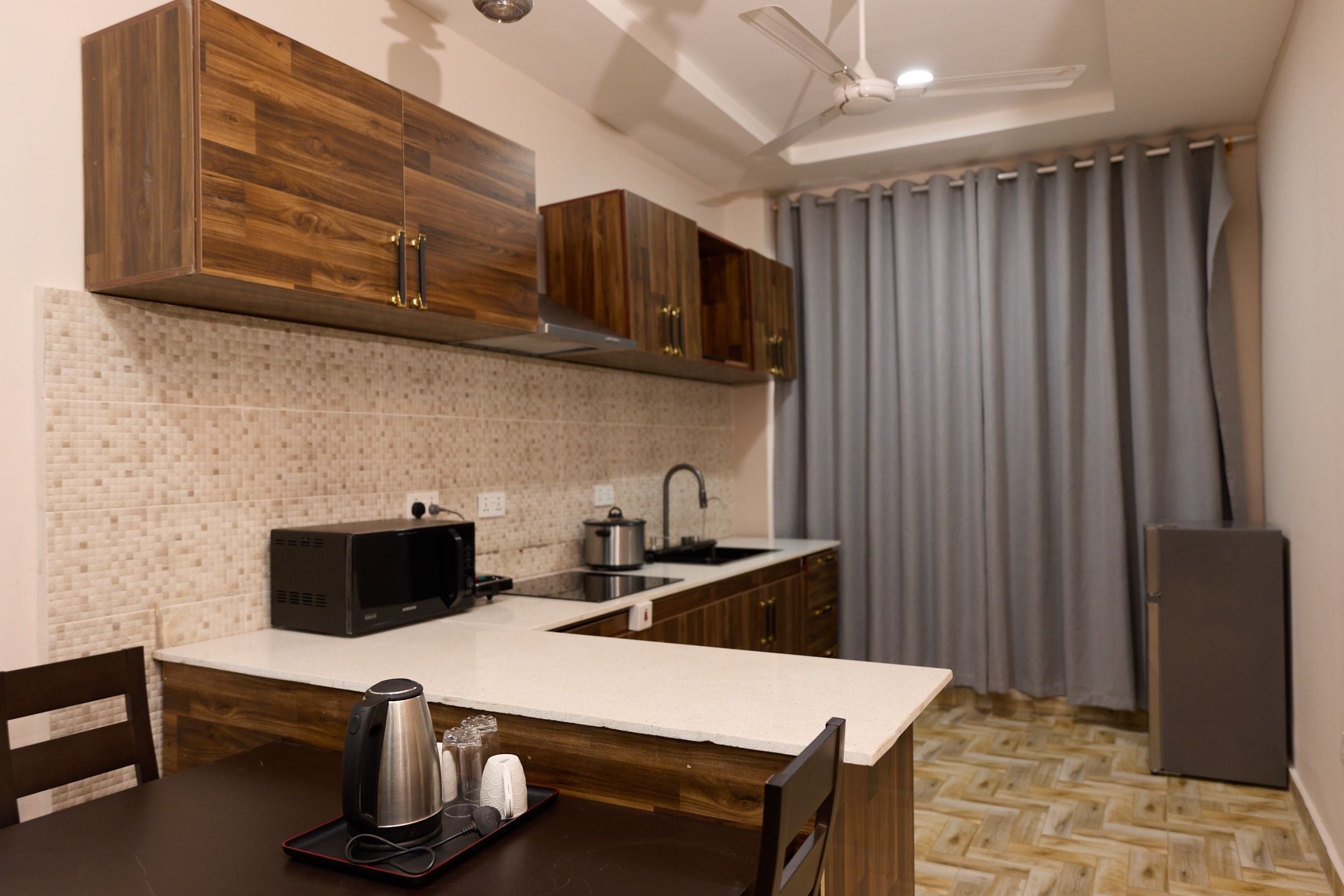 A compact kitchen with wooden cabinets, a microwave, a kettle, and a sink.