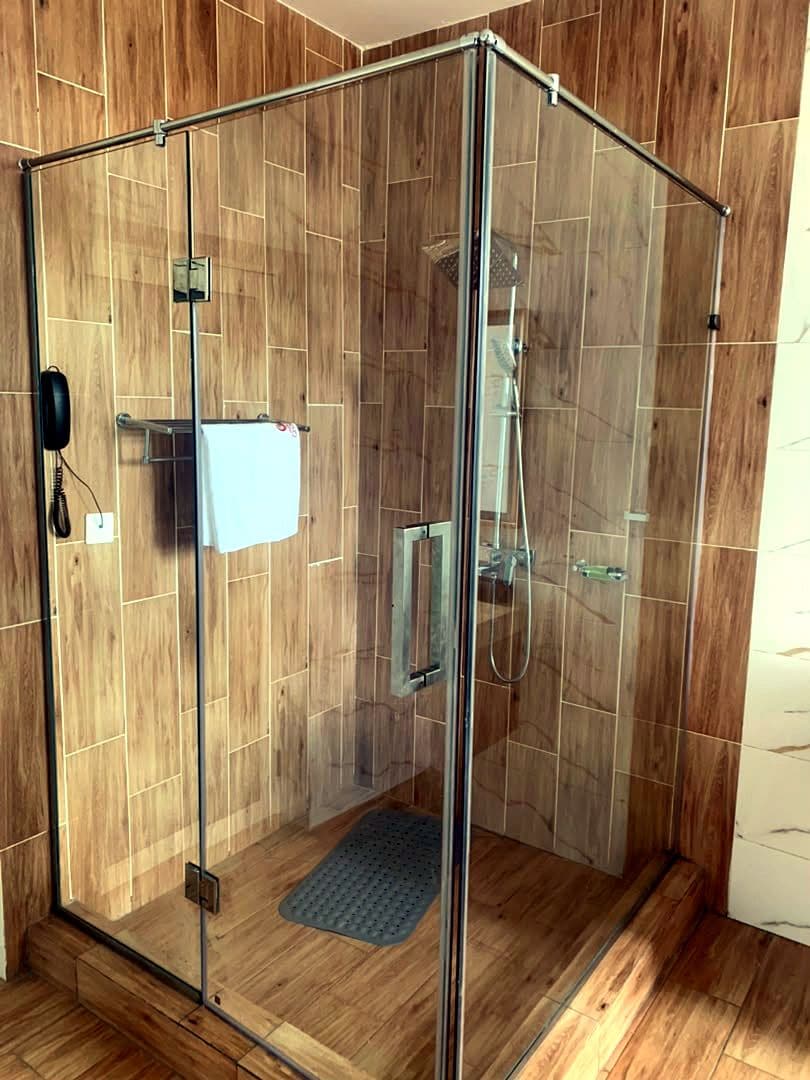Un box de ducha con paredes de vidrio, suelo de madera y un perchero para toallas.