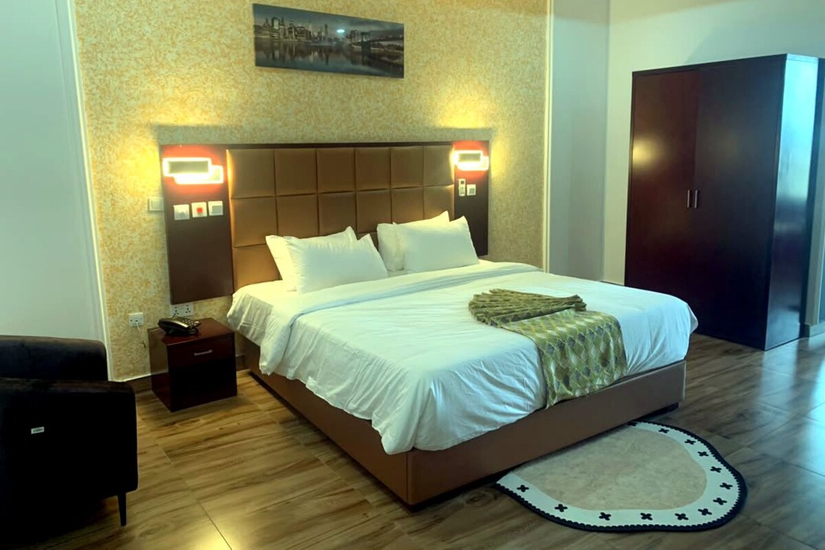 Una habitación de hotel con una cama grande, lámparas de noche, una mesita de noche, un armario y una fotografía de un paisaje urbano en la pared.