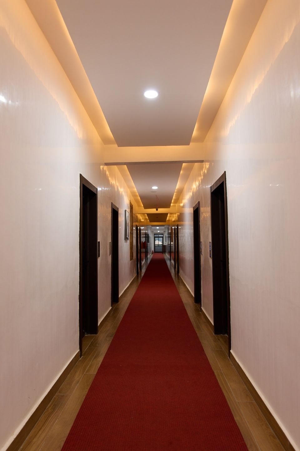 Un pasillo de hotel con alfombra roja, puertas a ambos lados y un techo con iluminación empotrada.