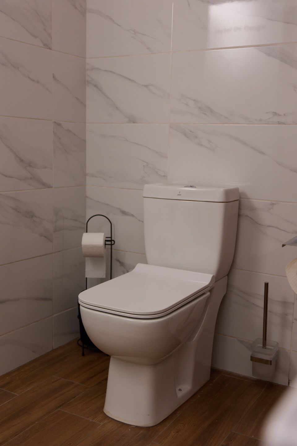 Une salle de bain avec des toilettes, des carreaux de marbre et un plancher en bois.