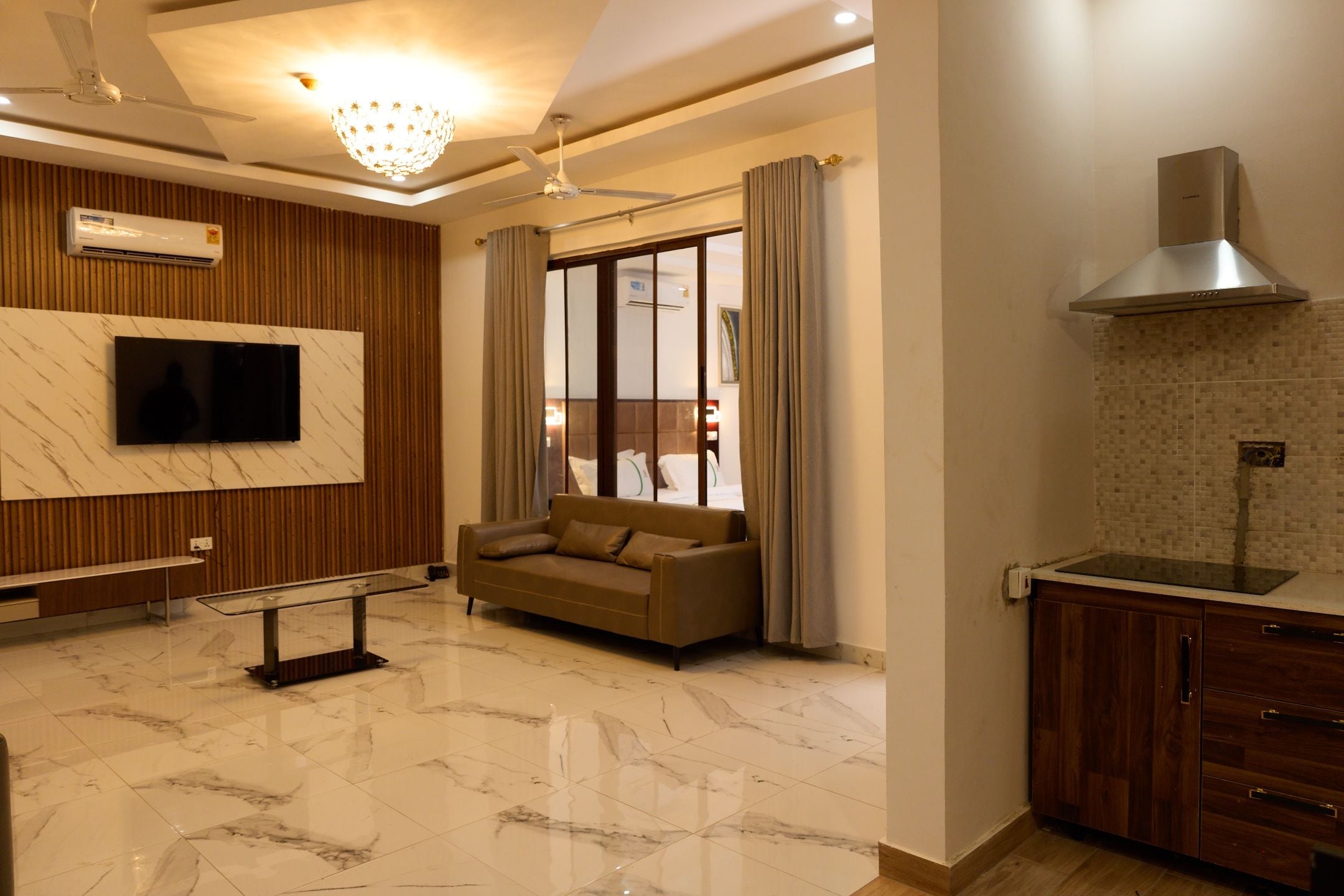 A modern living room with a sofa, a TV mounted on the wall, and a dining area with a kitchen counter.