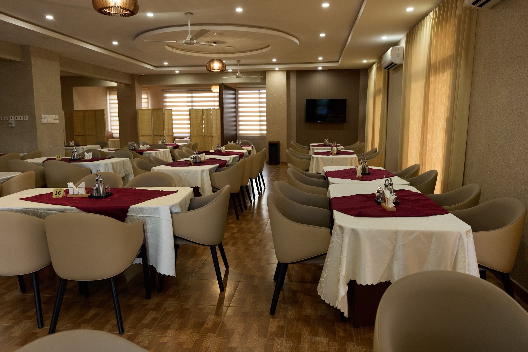 A restaurant with multiple tables, chairs, and a television screen on the wall.