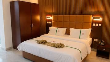A hotel room with a large bed, a wardrobe, a bedside table with a phone, and a wall-mounted light fixture.