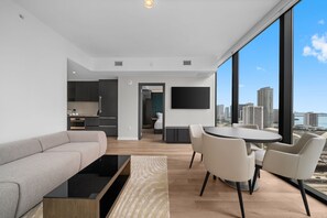A modern living room with a sofa, coffee table, and dining area with chairs, a TV mounted on the wall, and a view of the city through large windows. - Stunning Suite at E11EVEN Rooftop Pool Balcony Gym (Miami)