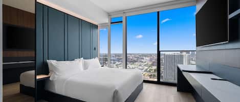 Un dormitorio moderno con una cama grande, televisor y vistas a la ciudad.