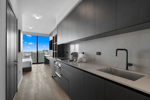 A modern kitchen with dark cabinetry, a large window, and a city view. - E11EVEN Studio Suite w/ Rooftop Pool City Views (Miami)