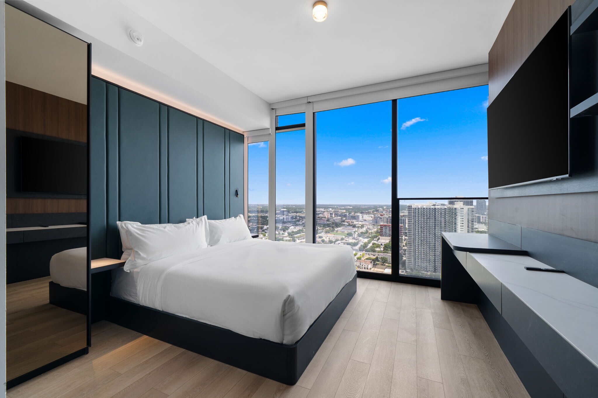 A modern bedroom with a large bed, a TV, and a city view.