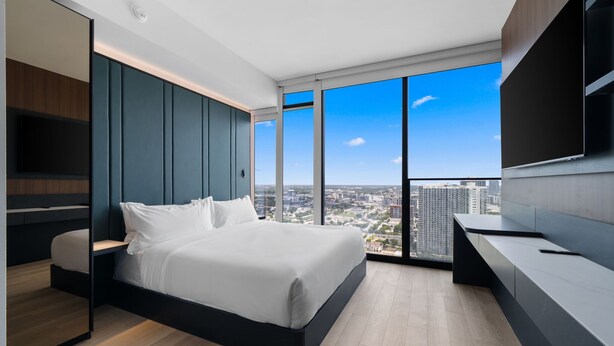 A modern bedroom with a large bed, a TV, and a city view. - E11EVEN Studio Suite w/ Rooftop Pool City Views (Miami)