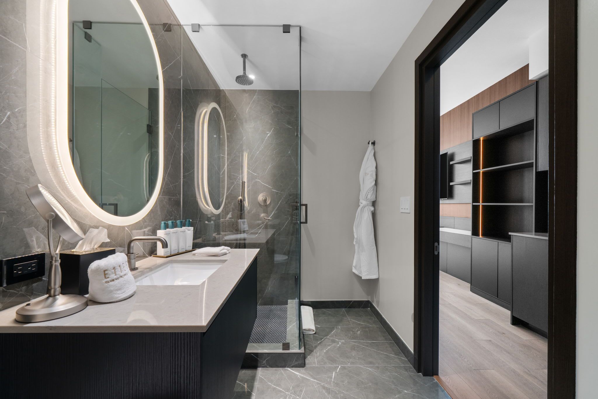 Een moderne badkamer met een douchecabine van glas, een grote spiegel en een wastafel met handdoek en toiletartikelen.