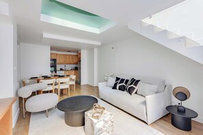 A modern living room with a sofa, coffee table, and chairs, a dining area with a table and chairs, and a kitchen with wooden cabinets and appliances. - Parisian Duplex 1br/6p - in the Heart of the Marais (Paris)