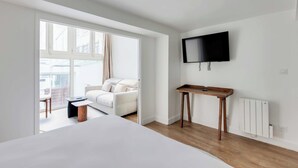 Moderni hotellihuone, jossa on sänky, pieni puinen yöpöytä, seinälle asennettu televisio ja suuri ikkuna, josta on näkymä ulos.