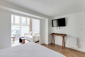 A modern hotel room with a bed, a small wooden side table, a TV mounted on the wall, and a view of the outside through a large window. - Parisian Duplex 1br/6p - in the Heart of the Marais (Paris)