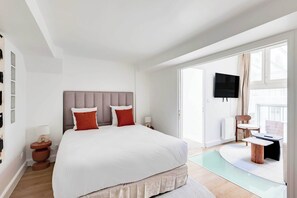 A modern hotel room with a large bed, a flat-screen TV, a seating area with a table and chairs, and a view of the outdoors. - Parisian Duplex 1br/6p - in the Heart of the Marais (Paris)