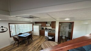 A compact kitchen with a microwave, stove, and sink, a dining area with a table and chairs, and a view through a doorway to a bathroom.