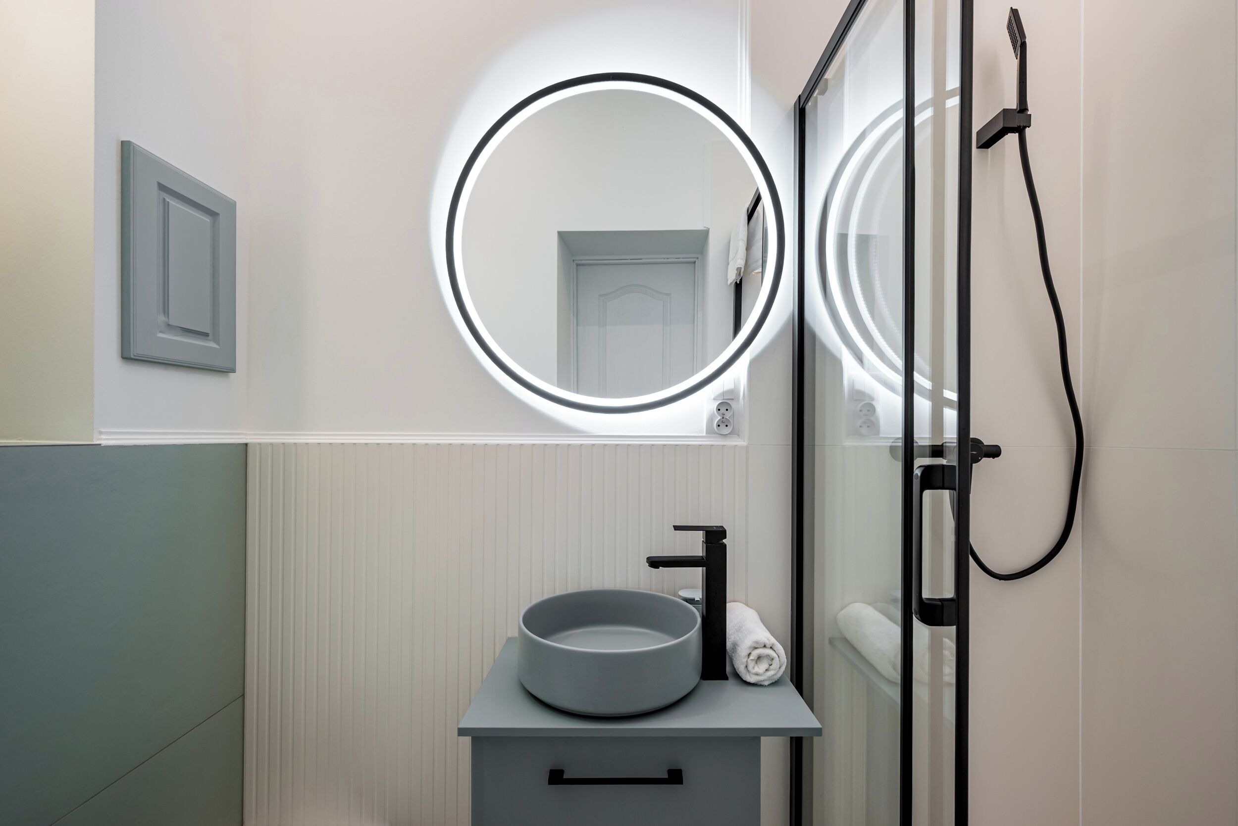 A modern bathroom with a round mirror, a sink with a bowl, and a shower.