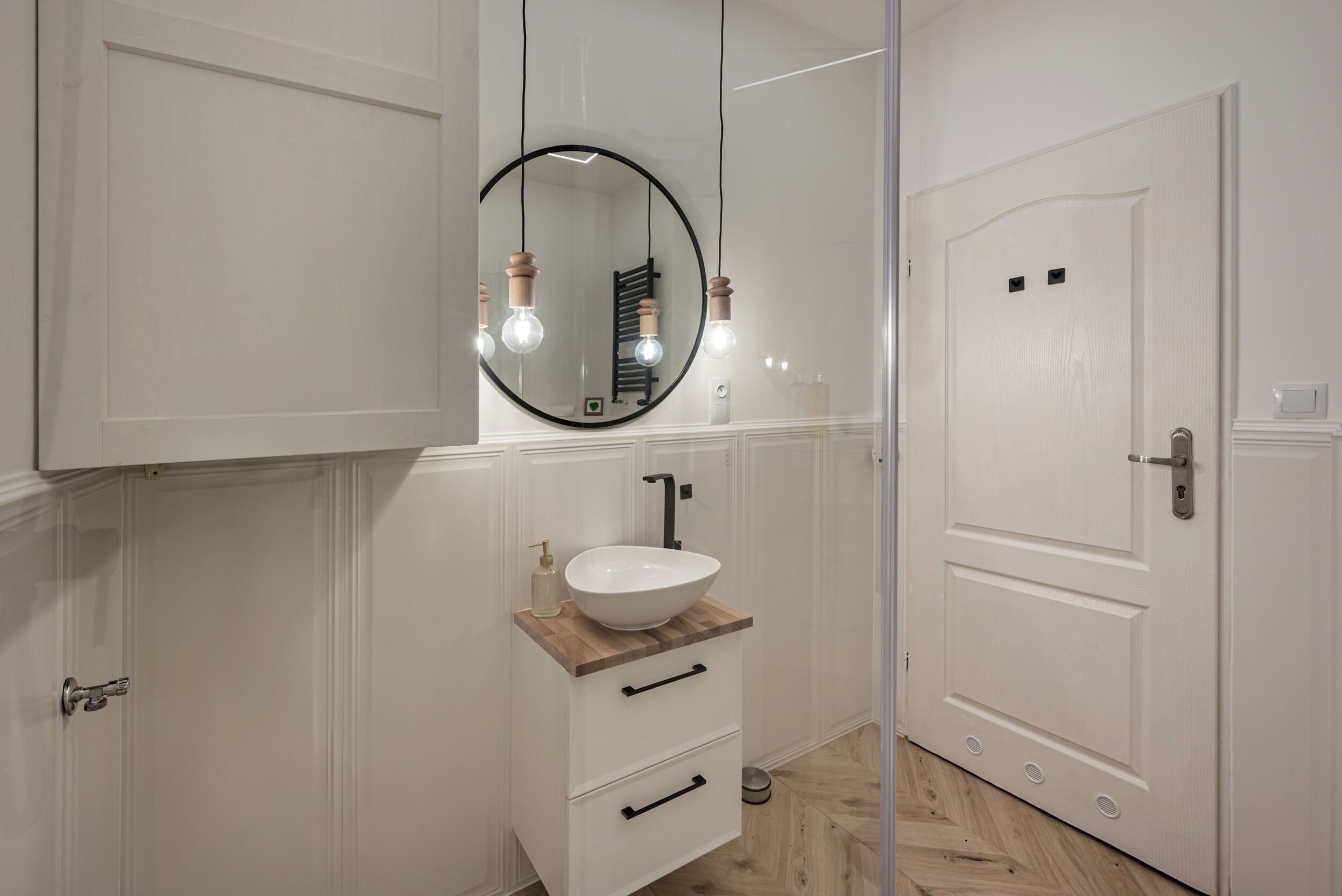 A bathroom with a white vanity, a round mirror, and a white sink.