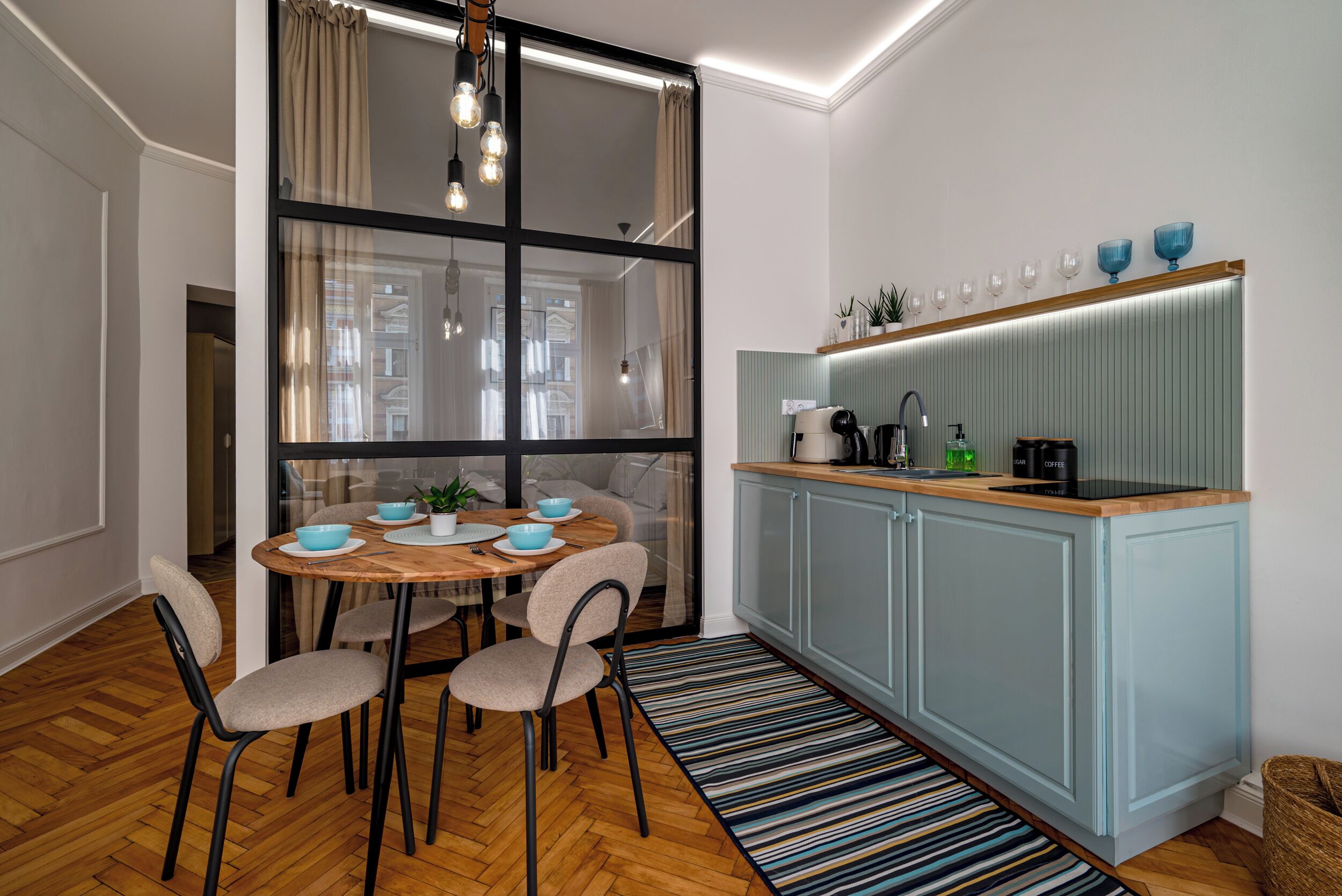 A modern kitchen with a dining area, featuring a round wooden table, chairs, and a striped rug.