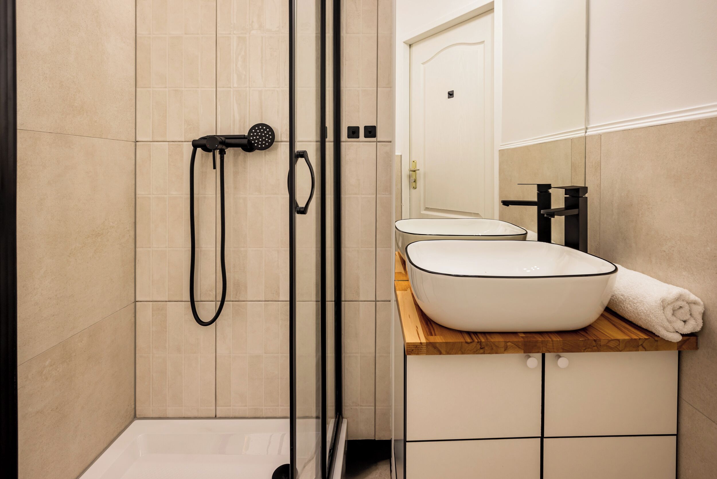A modern bathroom with a glass-enclosed shower, a white sink with a wooden countertop, and a mirror above the sink.