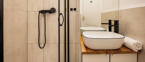 A modern bathroom with a glass-enclosed shower, a white sink with a wooden countertop, and a mirror above the sink.