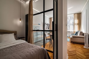 Una habitación de hotel moderna con cama, escritorio, silla y vistas de la ciudad a través de amplios ventanales.
