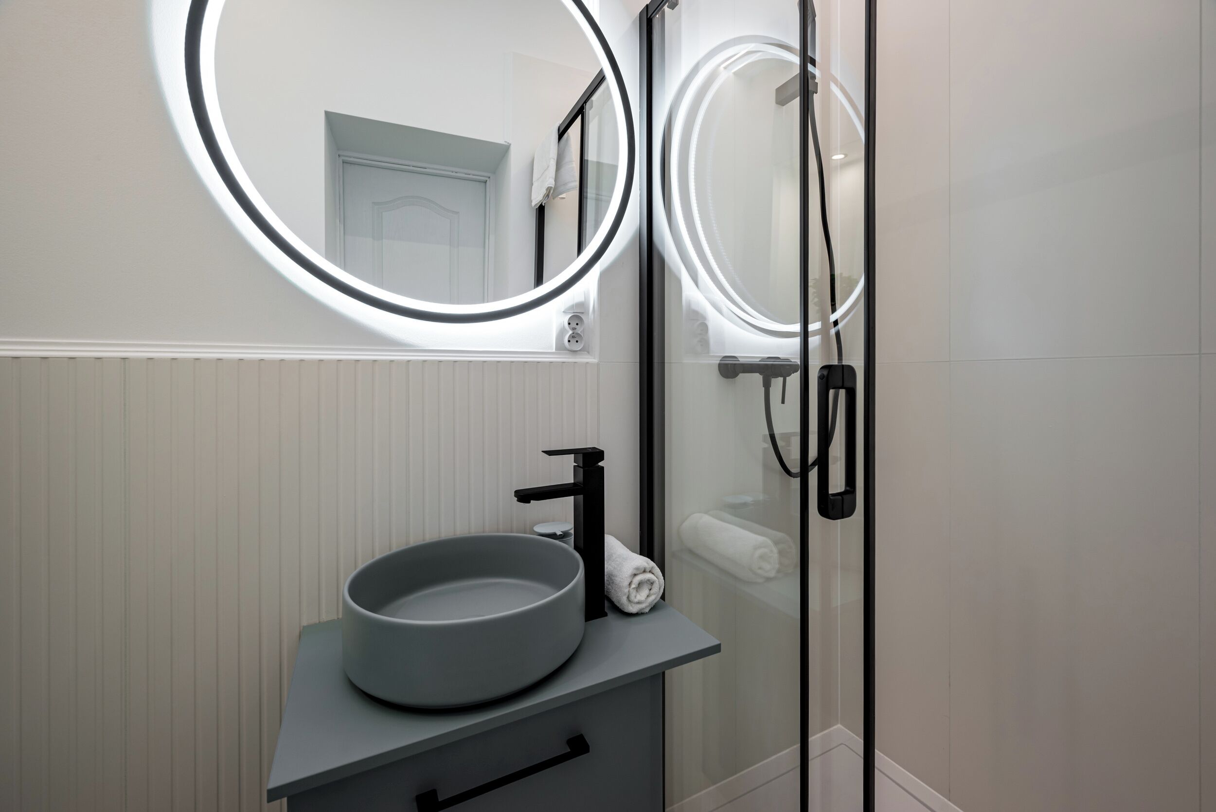 Un baño con un lavamanos moderno, un espejo con iluminación integrada y una zona de ducha.