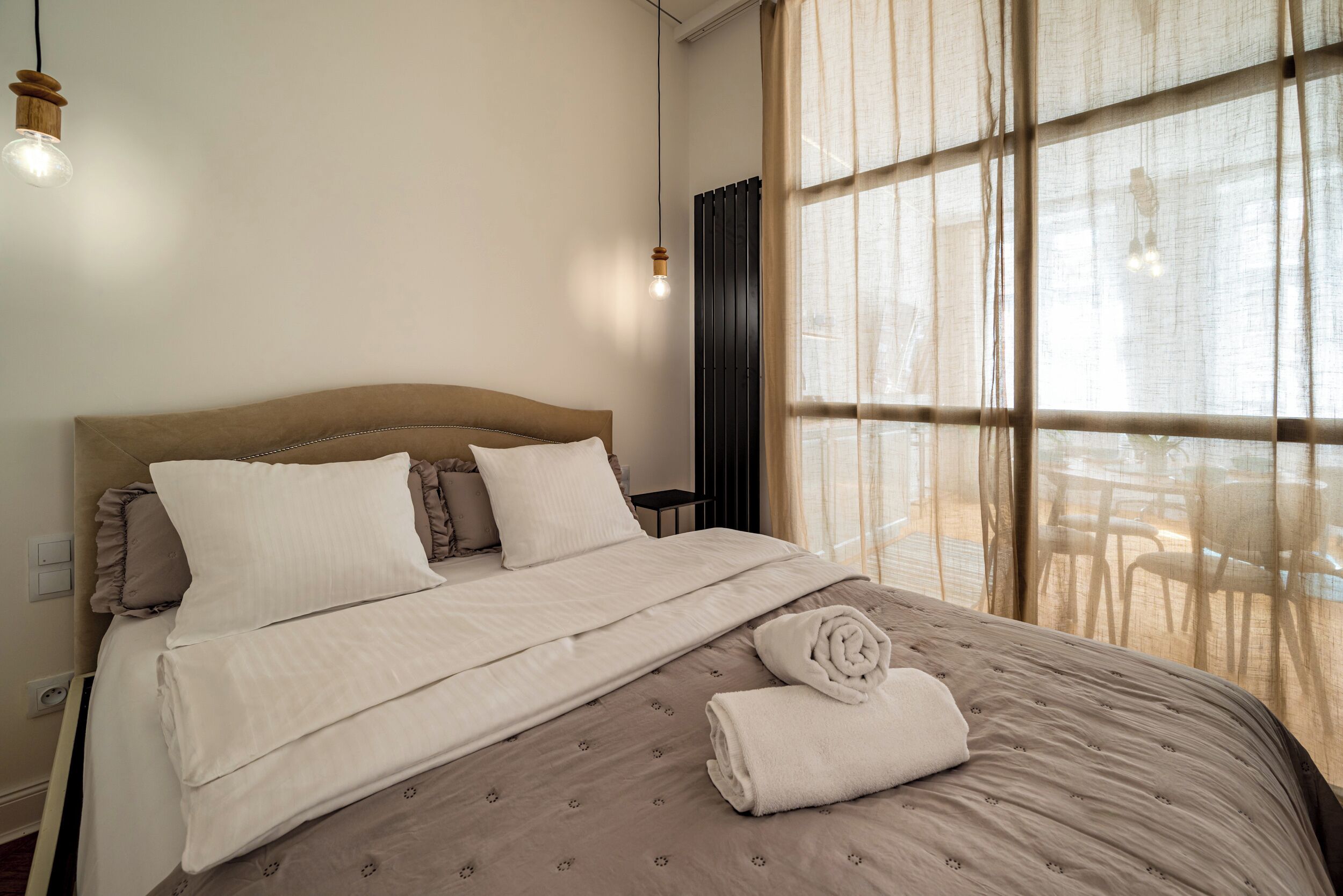 A neatly made bed with a duvet, pillows, and a rolled towel.