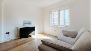 Una sala de estar minimalista con televisor de pantalla plana, una ventana con persianas y un sofá de color claro.