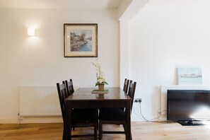 Ein Essbereich mit Tisch, Stühlen, einer Blumenvase, einem gerahmten Gemälde, einem Heizkörper und einem Fernseher.