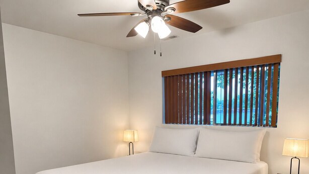 A bedroom with a bed, a ceiling fan, a window with blinds, and two bedside lamps.
