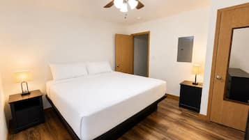 A bedroom with a bed, wooden flooring, a ceiling fan, and two bedside tables with lamps.