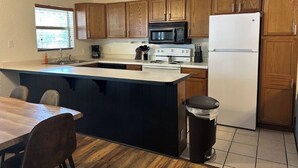 A kitchen with wooden cabinets, a microwave, a stove, a refrigerator, and a trash can.