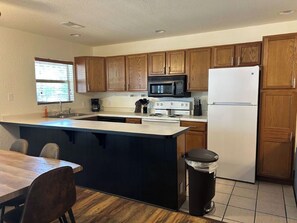 A kitchen with wooden cabinets, a microwave, a stove, a refrigerator, and a trash can.