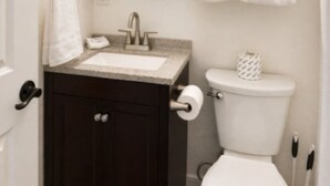 A bathroom with a white sink, dark cabinet, toilet, and a towel rack with towels.