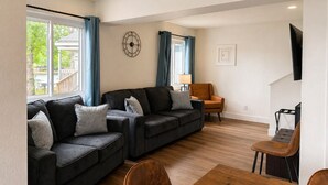 A modern living room with a sectional sofa, a dining table with chairs, and a television mounted on the wall.