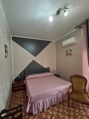 A bedroom with a bed, a chair, a wall-mounted air conditioner, and a painting.