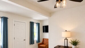 A room with a ceiling fan, a dark wooden dresser with drawers, a chair, and a television mounted on the wall.
