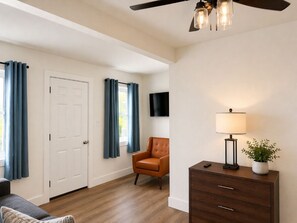 A room with a ceiling fan, a dark wooden dresser with drawers, a chair, and a television mounted on the wall.
