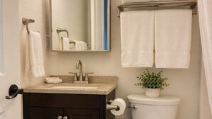 A bathroom with a white toilet, dark wooden vanity, a mirror, and a small potted plant.