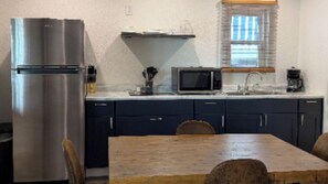 A compact kitchen with a refrigerator, microwave, and a wooden dining table. - Charming Cottage 1 at Alhonna Resort (Lake Ozark)